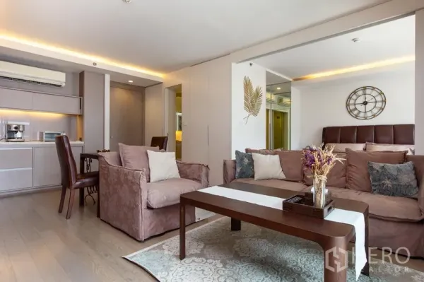 คอนโด ให้เช่าในWatthana, Bangkok - มุมนั่งเล่นอบอุ่น โซฟา โต๊ะกลาง และผนังกระจกเงาข้างครัว