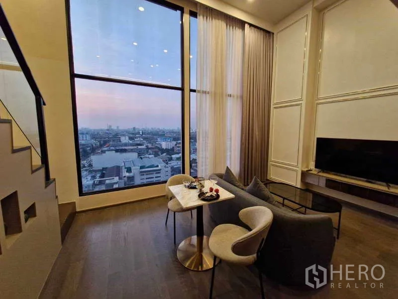 คอนโด ขายในRatchathewi, Bangkok - มุมนั่งเล่นวิวเมืองพาโนรามาผ่านหน้าต่างสูง พร้อมโซฟาและทีวี