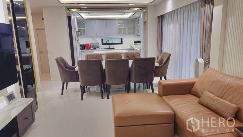 独立式住宅 出售在Sai Mai, Bangkok - 客餐一体空间，皮沙发与八人餐桌，落地窗帘旁。