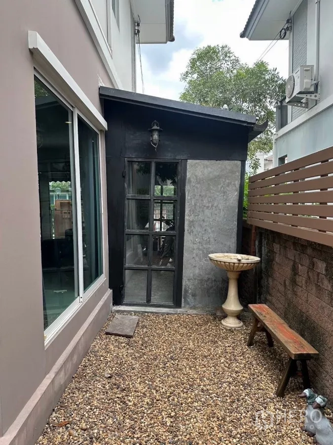 บ้าน ให้เช่าในSuan Luang, Bangkok - ลานกรวดข้างบ้าน ประตูห้องเก็บของสีดำ อ่างน้ำนก และม้านั่งริมรั้ว.