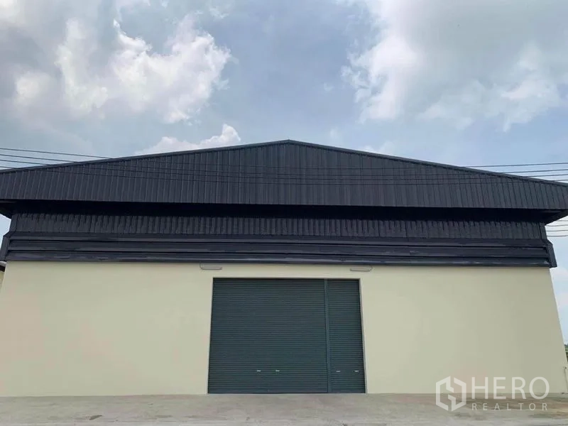 Warehouse for rent in Bang Bo, Samut Prakan - Front exterior of the warehouse with a large roller shutter door and wide driveway.