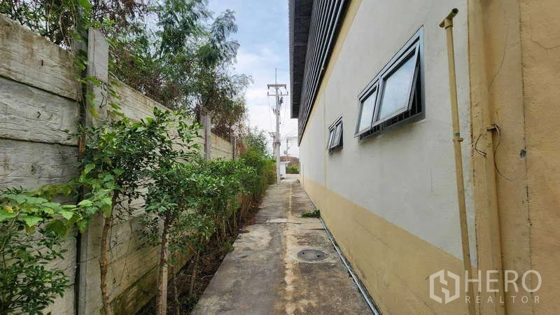 货栈 出租在Ban Phaeo, Samut Sakhon - 仓库侧边通道，设小窗、绿植与围墙