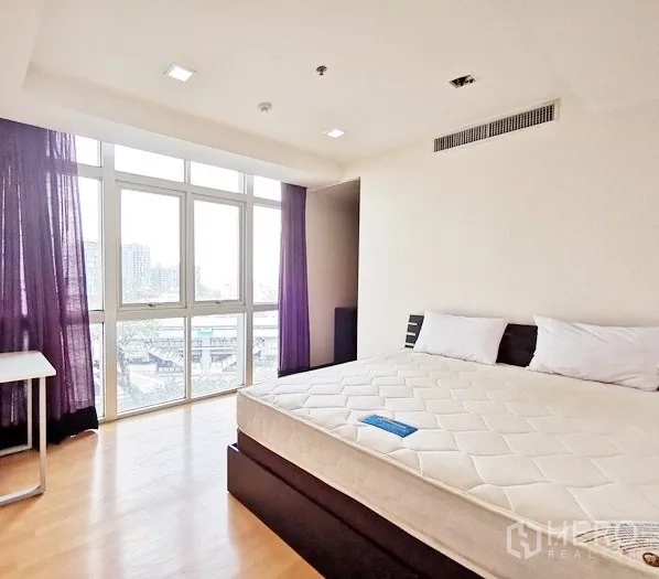 公寓 出租在Khlong Toei, Bangkok - 转角卧室，落地窗享城市景观，木地板与大床。