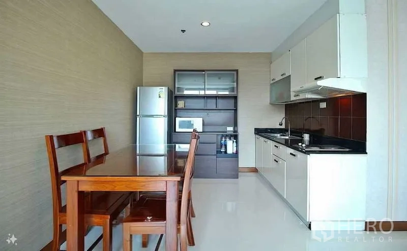 Condominium for sale in Watthana, Bangkok - Open-plan kitchen with white cabinets, black countertops, wooden dining set and stainless refrigerator.