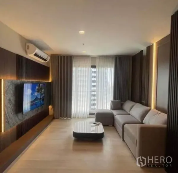 Condominium for rent or sale - Modern living room with L-shaped sofa, TV feature wall and floor-to-ceiling curtains.