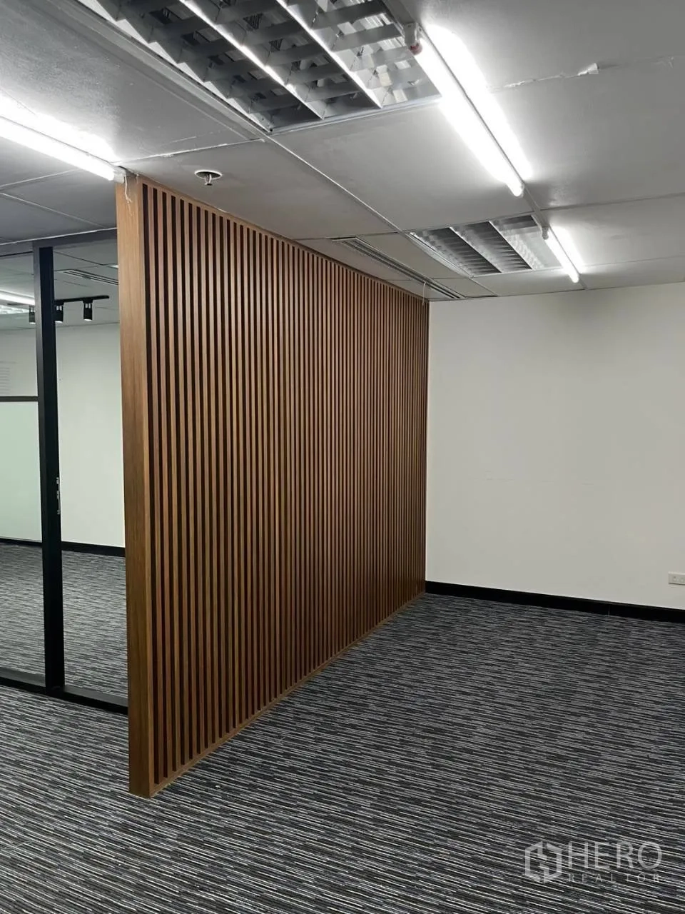 Office Space for rent in Khlong Toei, Bangkok - Wood slat feature partition in a carpeted workspace with fluorescent lighting.