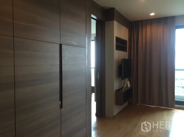 公寓 出租在Bang Rak, Bangkok - 起居区带内置柜、壁挂电视和落地窗帘，可通往阳台。