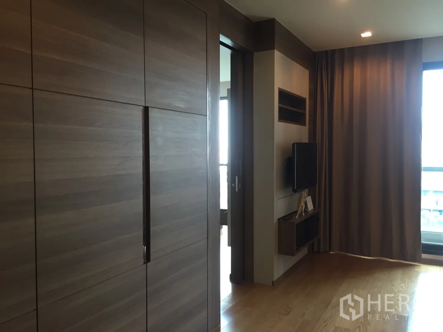 公寓 出租在Bang Rak, Bangkok - 起居区带内置柜、壁挂电视和落地窗帘，可通往阳台。