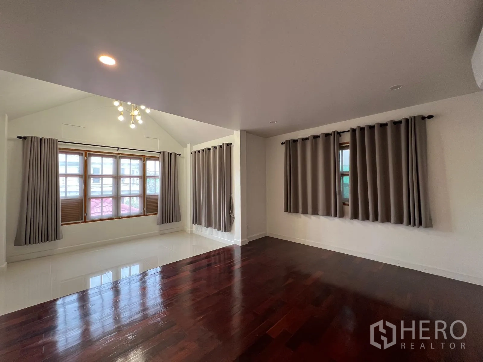Detached House for rent in Saphan Sung, Bangkok - Corner perspective of a large living space with hardwood floors and multiple curtained windows.