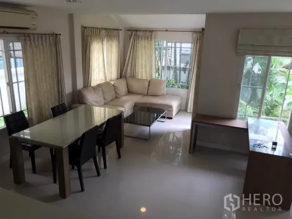Detached House for rent in Khlong Sam Wa, Bangkok - Bright living area with L-shaped sofa, dining table and windows looking to the green garden.