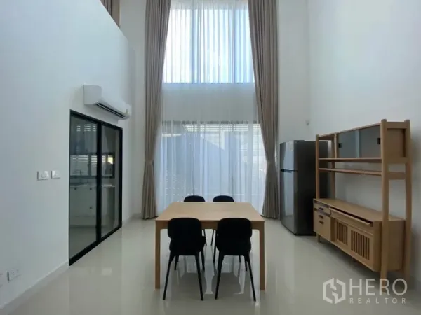 Townhouse for rent in Saphan Sung, Bangkok - Bright double-height dining area with floor-to-ceiling curtains, wooden table, and built-in shelving.