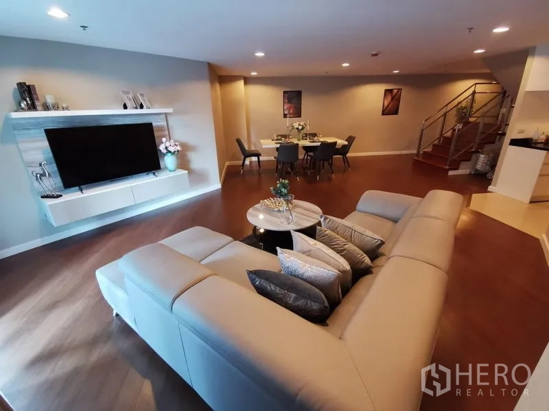 Condominium for rent or sale in Huai Khwang, Bangkok - Spacious duplex living room with L-shaped sofa, TV wall, dining area and staircase.
