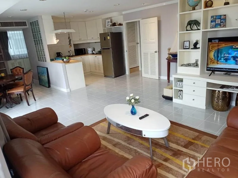 คอนโด ให้เช่าหรือขายในWatthana, Bangkok - ห้องนั่งเล่นแบบโอเพ่นพร้อมโซฟาหนังสีน้ำตาล ผนังทีวีบิลท์อิน และครัวเชื่อมต่อ