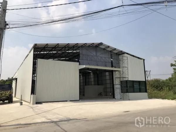 Warehouse for rent in Pak Kret, Nonthaburi - Front facade with roll-up door, canopy and ample concrete forecourt for truck parking.