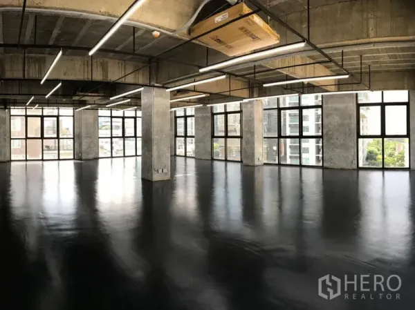 Office Space for rent in Khlong Toei, Bangkok - Open-plan loft office with polished black epoxy floor, exposed concrete ceiling, linear LED lights, and full-height windows with city views in Phrom Phong.