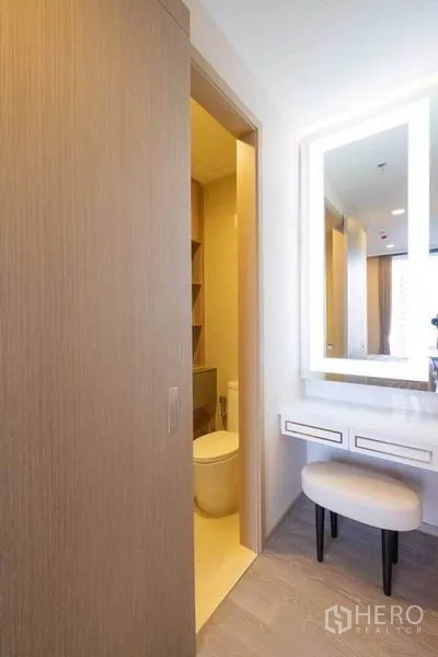Condominium for rent in Watthana, Bangkok - Vanity corner with backlit mirror and stool next to sliding door bathroom.