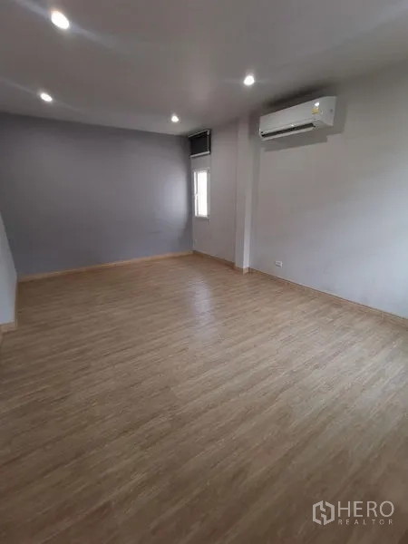 Detached House for rent in Chatuchak, Bangkok - Large multipurpose room with AC, grey accent wall, and laminate wood flooring.