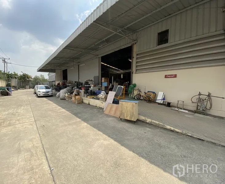 Factory for sale in Khlong Luang, Pathum Thani - Warehouse frontage with open roller doors, loading dock and a wide driveway for trucks.