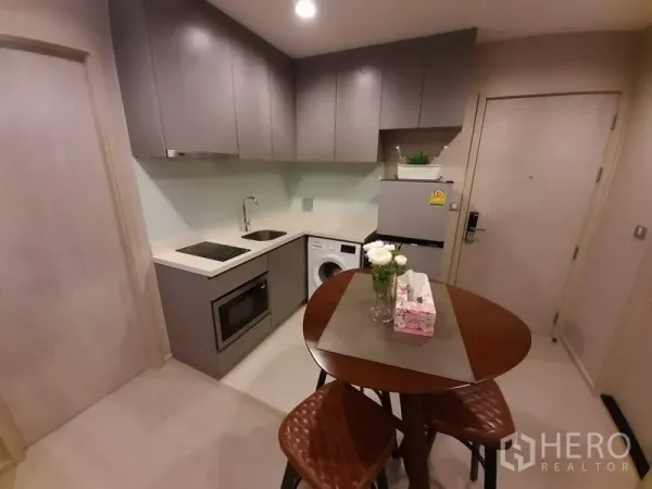 คอนโด ให้เช่าหรือขายในKhlong Toei, Bangkok - ครัวรูปตัวแอลตู้สีเทา พร้อมเตาไฟฟ้า ไมโครเวฟ เครื่องซักผ้า และตู้เย็น