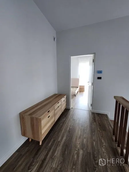 Detached House for rent in Bang Kapi, Bangkok - Upstairs corridor with wooden sideboard and wood flooring leading to a bright bedroom.