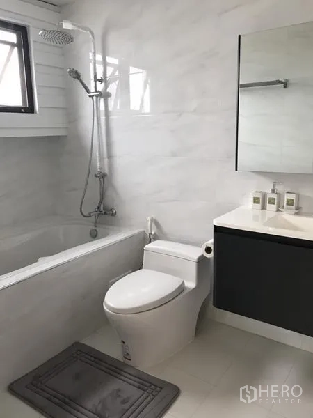 公寓 出租在Bang Rak, Bangkok - 浴室带浴缸与顶喷花洒、带镜洗手台、白色瓷砖和小窗。