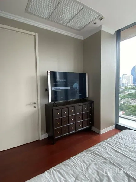 Condominium for rent in Watthana, Bangkok - Bedroom corner with TV on a cabinet and a wide window framing a city view.