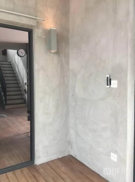 Detached House for sale in Pak Kret, Nonthaburi - Entrance nook with textured concrete wall, wall light and a sliding door leading toward the staircase.