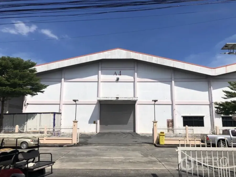 货栈 出租 - 白色人字顶仓库外立面，中央A4卷闸门与坡道，封闭园区内，蓝天下。