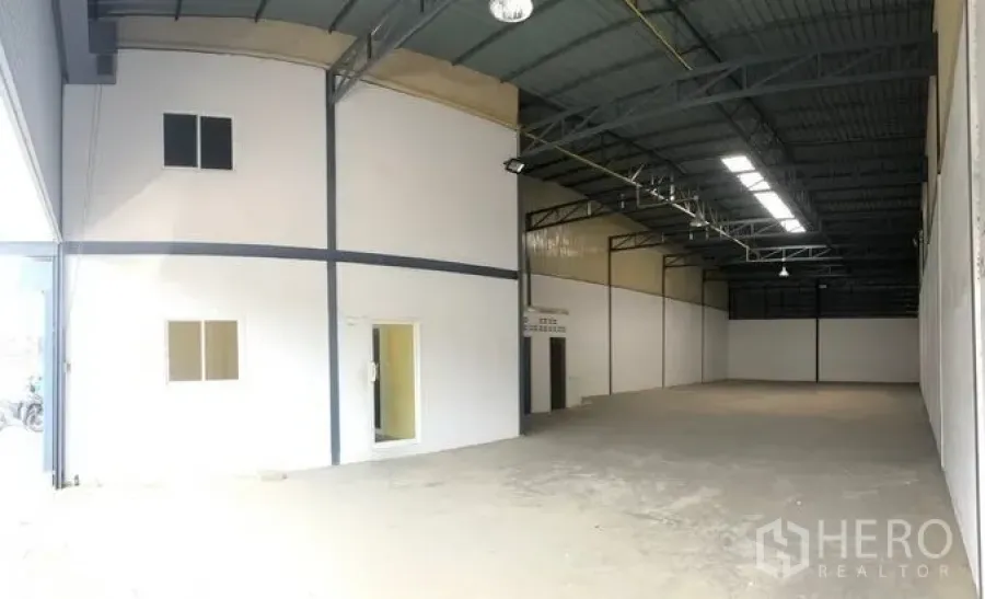 Warehouse for rent in Pak Kret, Nonthaburi - Spacious warehouse interior with high steel roof, skylight panels, and a white partitioned office.
