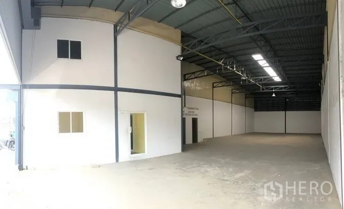 Warehouse for rent in Pak Kret, Nonthaburi - Spacious warehouse interior with high steel roof, skylight panels, and a white partitioned office.