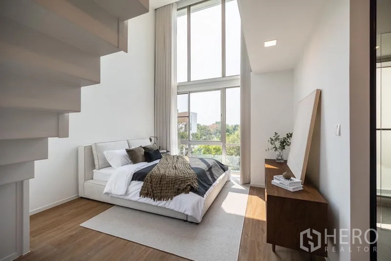 Detached House for rent in Saphan Sung, Bangkok - Double-height bedroom beneath the staircase with tall windows and garden outlook.