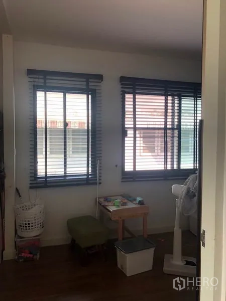 Townhouse for sale in Phasi Charoen, Bangkok - Bright corner room with two windows, blinds and small seating area.