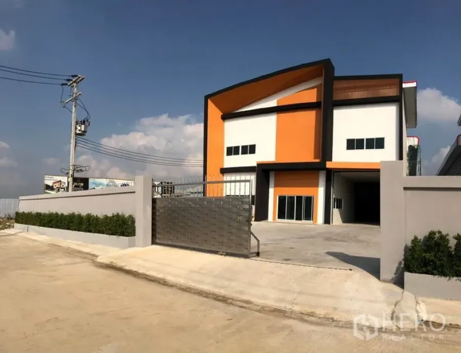 Factory for rent or sale in Krathum Baen, Samut Sakhon - Gated modern two-storey factory with orange and white facade, wide concrete driveway and perimeter wall in Krathum Baen, Samut Sakhon.