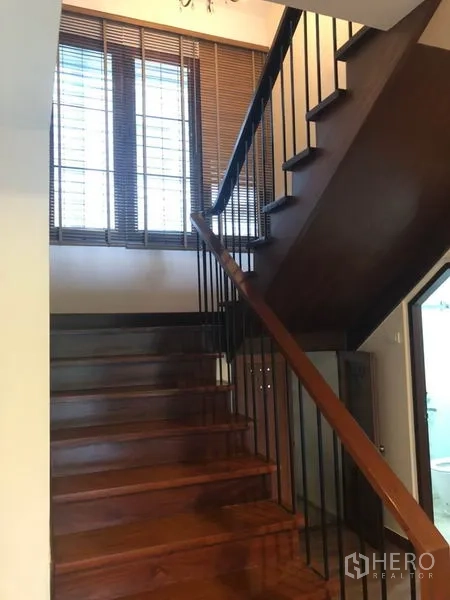 Detached House for rent in Watthana, Bangkok - Staircase with wooden treads and black metal balustrade beside window blinds.