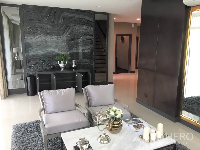 Detached House for rent or sale in Bang Kapi, Bangkok - Living area featuring a marble accent wall, lounge chairs and a view to the staircase corridor.