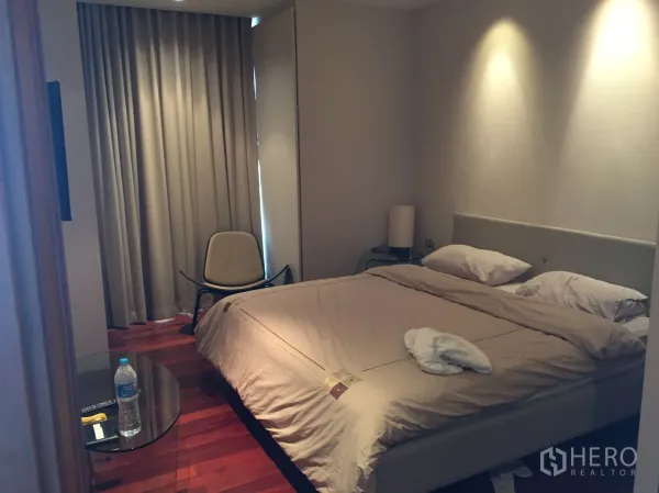 Condominium for rent in Sathon, Bangkok - Second bedroom with warm lighting, blackout curtains and polished wooden flooring.