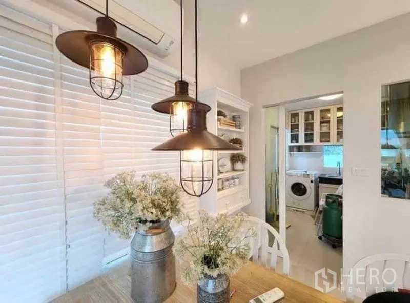 Detached House for rent in Bang Bo, Samut Prakan - Dining table under industrial pendant lights beside doorway to the kitchen.