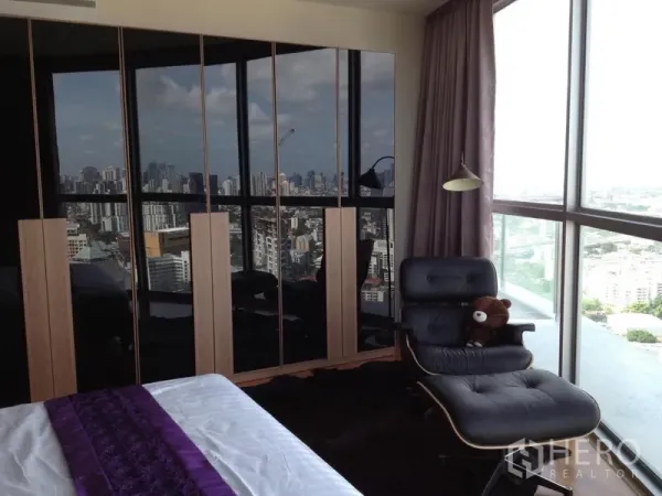 คอนโด ให้เช่าในWatthana, Bangkok - มุมห้องนอนชมวิวสกายไลน์ผ่านกระจกสูง พร้อมตู้เสื้อผ้าบานเงาและเก้าอี้เอน
