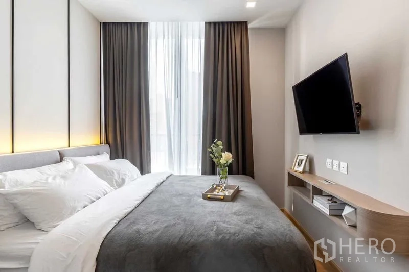 Condominium for rent in Watthana, Bangkok - Bedroom with wall-mounted TV and tall curtains over a full-height window.