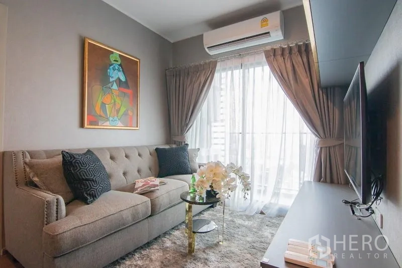 Condominium for rent in Phra Khanong, Bangkok - Lounge with balcony access, sheer curtains and wall-mounted TV.