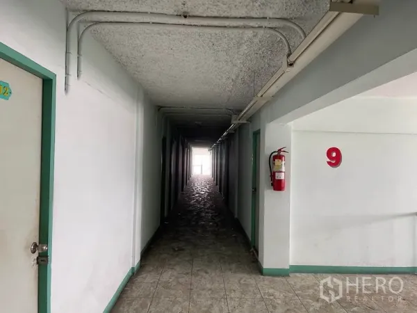 Apartment for sale in Mueang Samut Prakan, Samut Prakan - Long hallway with number nine marker and a wall-mounted fire extinguisher.