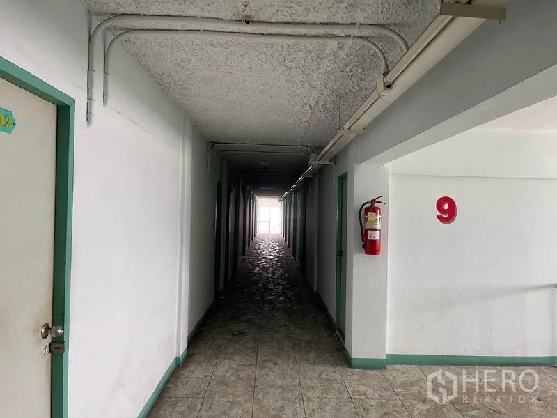 Apartment for sale in Mueang Samut Prakan, Samut Prakan - Long hallway with number nine marker and a wall-mounted fire extinguisher.