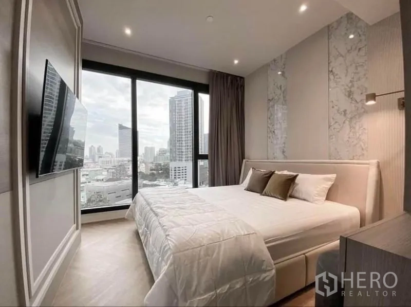 Condominium for rent in Din Daeng, Bangkok - Master bedroom with marble accent wall, king bed and wall-mounted TV facing the skyline.