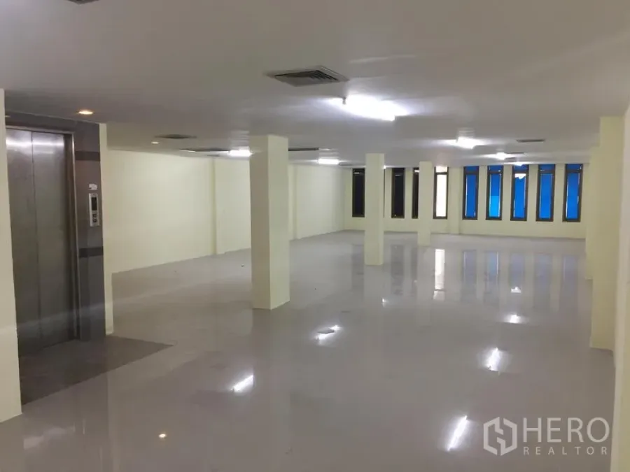 Home Office for rent in Watthana, Bangkok - Open workspace with structural columns, fluorescent lighting, long row of windows and an elevator lobby.