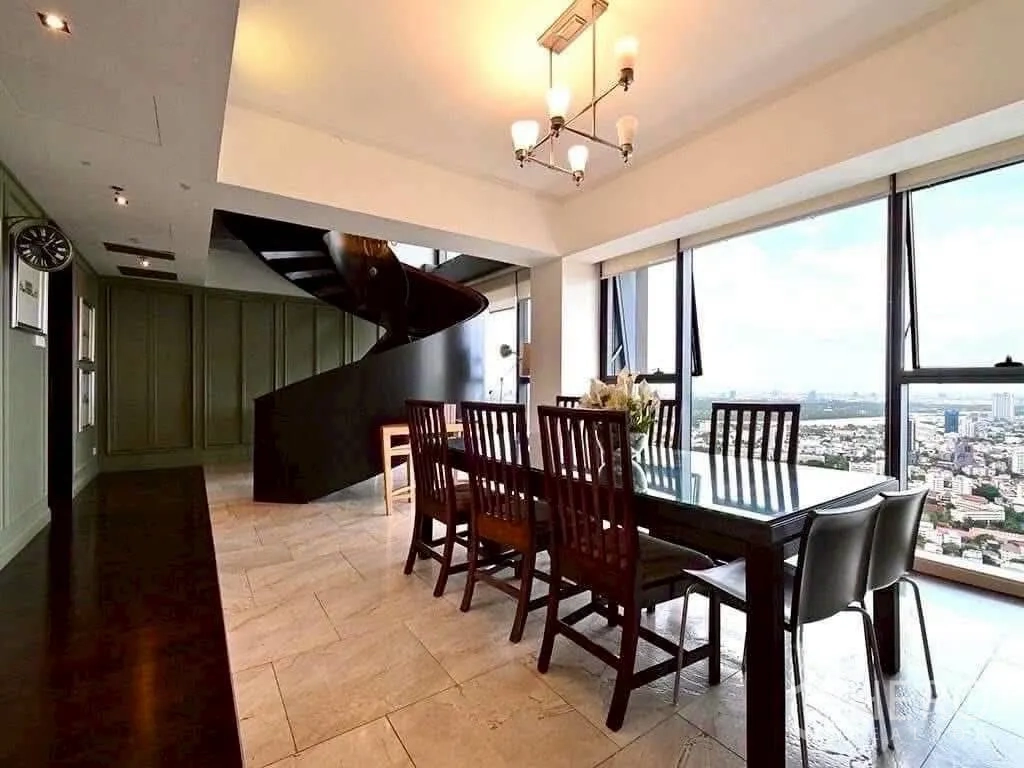 Condominium for rent in Sathon, Bangkok - High-floor dining area with glass table, chandelier and spiral staircase beside floor-to-ceiling windows showing city and river views.