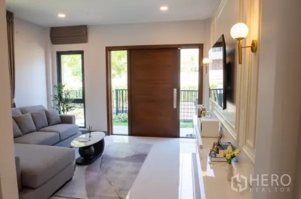 Detached House for rent in Bang Phli, Samut Prakan - Bright living room featuring a gray sofa, TV wall and large wooden sliding door to the garden.