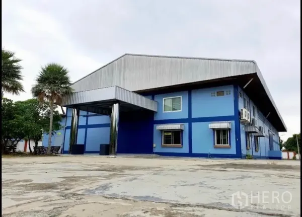 Factory for sale in Chon Buri - Close-up of blue warehouse exterior with covered loading area and yard