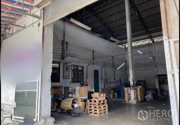 Warehouse for rent in Bang Khun Thian, Bangkok - Warehouse loading entrance showing roller door, small internal office area, pallets, and utility lines.