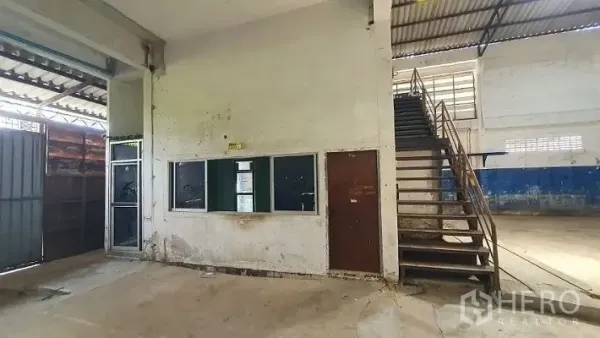 Warehouse for rent in Phra Samut Chedi, Samut Prakan - Ground-floor office block with windows and a metal stair up to an upper office beside a large sliding gate.