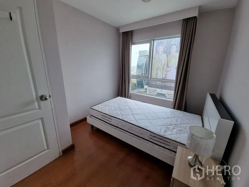 Condominium for rent in Huai Khwang, Bangkok - Secondary bedroom with bed by the window and city view.